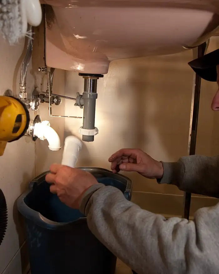 A plumber fitting pipework under a sink